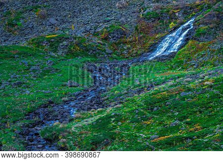 Waterfall On A Mountain Slope Flowing Through Green Grass And Moss Growing On The Rocks.