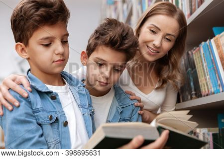 Two Adotable Young Twin Brothers And Their Charming Mom Enjoying Reading A Book Together At The Libr