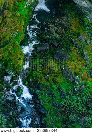 Waterfall Running Through A Deep Gorge Surrounded By Lush Green Vegetation. Seen From Above.