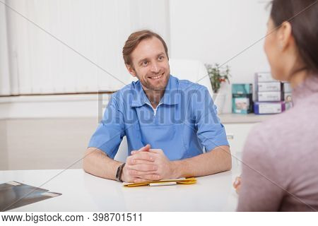 Cheerful Mature Male Doctor Smiling At His Female Patient During Medical Consultation