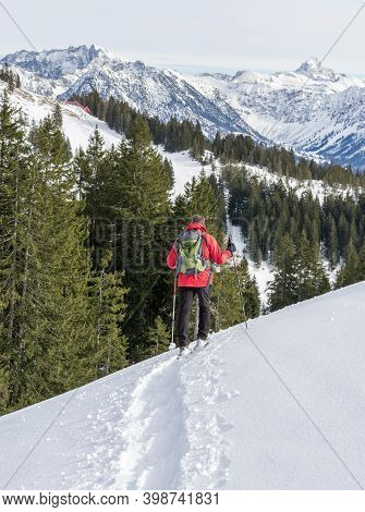 Senior Man Is Snowshoe Hiking In Alpine Snow Winter Mountains. Allgau, Bavaria, Germany.