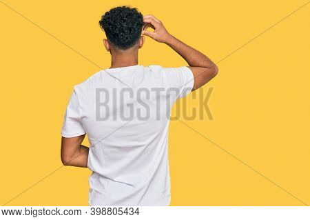 Young arab man wearing casual white t shirt backwards thinking about doubt with hand on head 