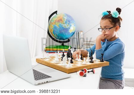 Portrait Caucasian Little Cirly Girl Playing Chess At The Table In Interior With Chessboard. Little 