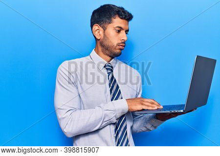 Young latin man holding laptop thinking attitude and sober expression looking self confident 