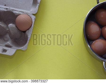 Beige Boiled Eggs In A Pot Of Water With An Egg Box On A Gray Background. High Quality Photo