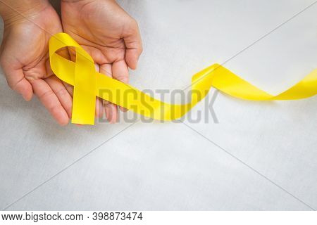 Hand Holding Yellow Ribbon On White Background, Copy Space. Bone Cancer, Sarcoma Awareness, Childhoo