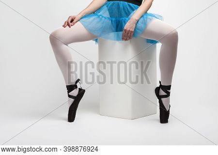 Closeup Of Legs Of Caucasian Female Ballet Dancer In Pointes Shoes And Blue Skirt Sitting On High Cu