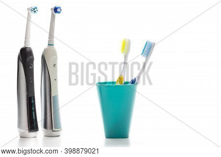 Pair Of Professional Electric Toothbrushes In Front Of Two Manual Tooth Brushes In One Cup On White