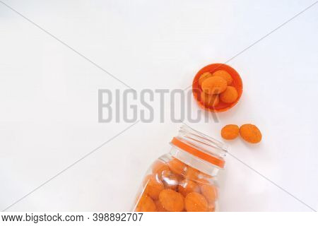 Peanuts In Orange Glaze Are Spil From A Jar On A White Background, Copy Space