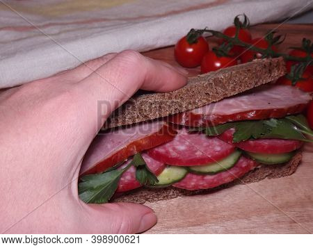 Hand Holding A Sandwich With Different Varieties Of Sausage And Vegetables. High Quality Photo