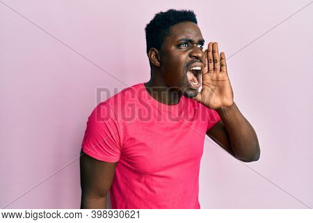Handsome black man wearing casual pink t shirt shouting and screaming loud to side with hand on mouth. communication concept. 