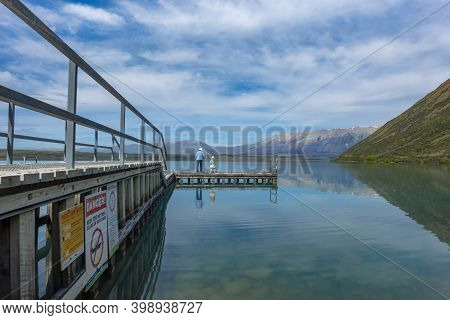 Lake Ohau New Zealand - November 12 2020; Jetty On Lake Ohau Reflections With Woman And Child Standi