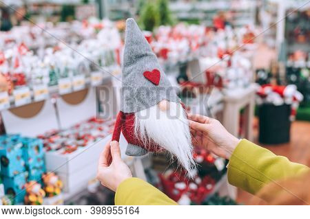 The Girl Holds Tomte In Her Hands. Against The Background Of The Counter Of The Christmas New Year's