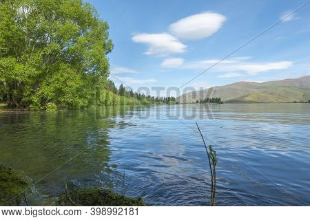 Lake Ruataniwha Edge With Lime Green Spring Growth On Willow Trees Running Along Length Of Water's E