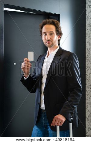 Young business man standing with a keycard in front of a room door in a hotel