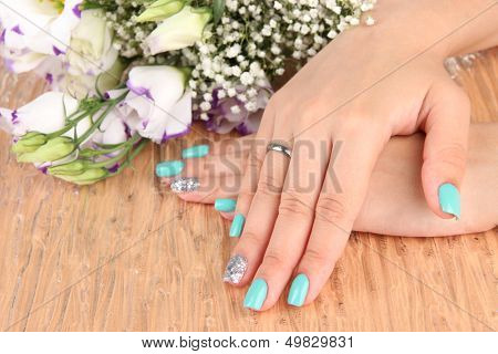 Beautiful woman hands with blue manicure near bouquet of beautiful flowers, on color background