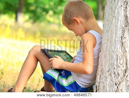 Boy Child Playing With Tablet Pc Sitting On Skateboard Outdoor With Forest On Background Game Depend