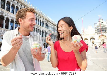 Couple eating ice cream on vacation travel in Venice, Italy. Smiling happy young couple in love having fun eating italian gelato food outdoors during holidays on San Marco Square, Venice, Italy