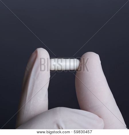 Hand in white latex glove holding white capsule