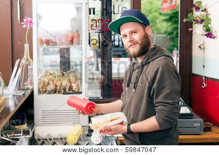 Hotdog - friendly salesman and fresh ingredients in a fast food snack bar