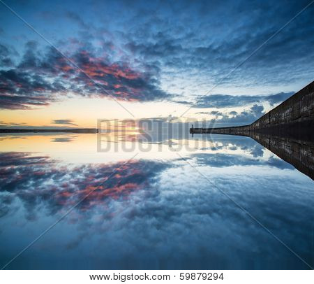 Beautiful Vibrant Sunrise Sky Over Calm Water Ocean With Lighthouse And Harbor Wall