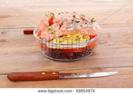 fresh fried natural pink salmon on italian traditional tagliatelle backed with tomato and vegetables served over wooden table with cutlery