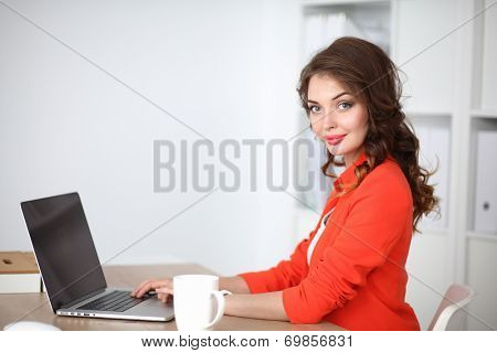 Attractive woman sitting at desk in office, working with laptop computer