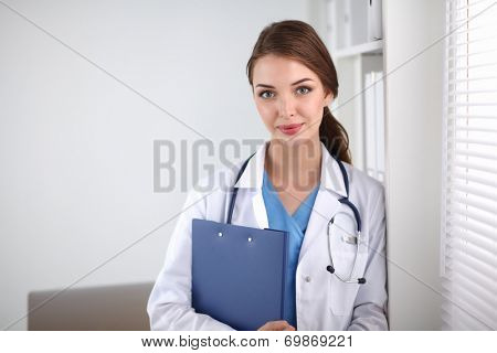 Young woman is standing in the near window with folder