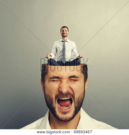 portrait of stressed young man with open head. calm businessman sitting in yoga asana and smiling in the man's head. photo over grey background