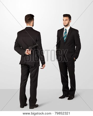 Two opposing businessman shake hands, one of them hiding a weapon behind his back