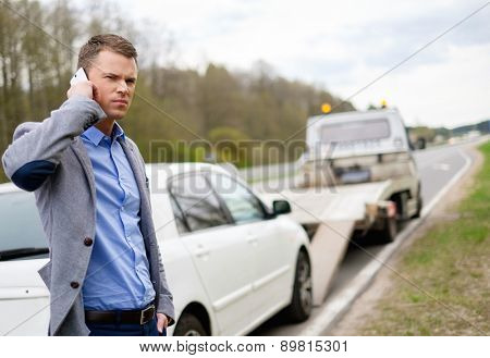 Man calling while tow truck picking up his broken car 