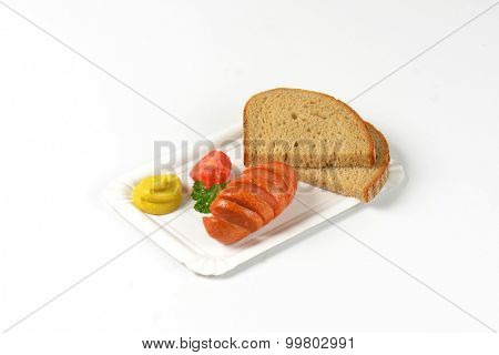roasted sausage, mustard and bread slices on paper plate