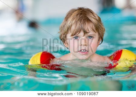 little kid boy with swimmies learning to swim in an indoor pool