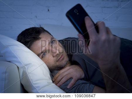 Young Man In Bed Couch At Home Late At Night Using Mobile Phone In Low Light Relaxed In Communicatio