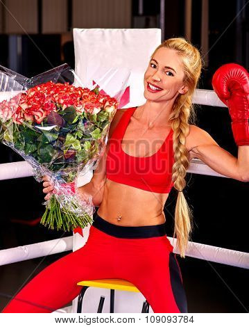 Happy girl boxer wearing red gloves with bouquet flowers sitting in corner of boxing ring.