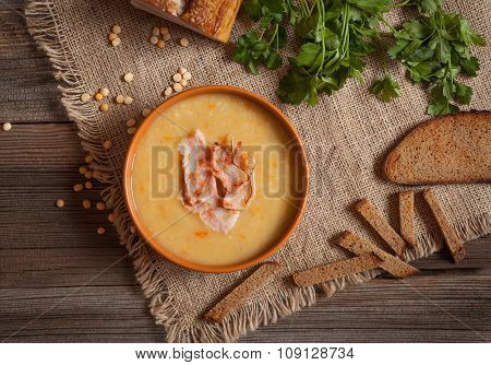 Pea soup traditional German dinner foood with greens, bacon and croutons in clay dish on vintage woo