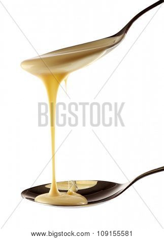 Condensed milk pouring from spoons, isolated on white