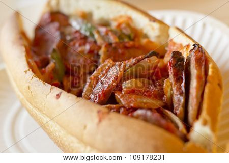 Fried sausage onions and red and green bell peppers on sandwich bun