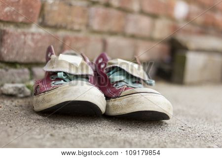 Pair of old smelly worn classic sneakers leaning against a brick wall