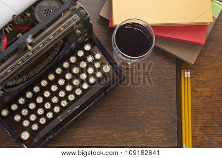 Old vintage typewriter with glass of wine pencils and books in this retro creative writing and relazation themed desk top