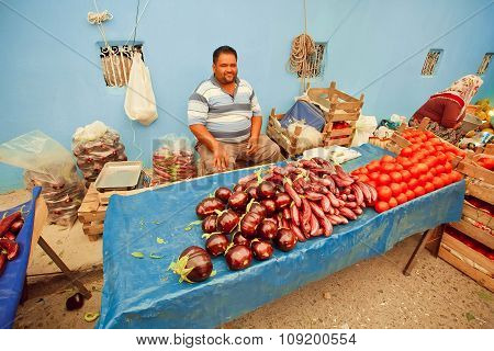 Happy Vegetable Trader Waiting For Customers With Eggplant And Tomatoes On Rural Market In Turkey