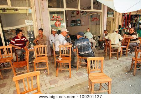 Senior Men Sitting Around Tables And Talking In Rustic Cafe Of Village