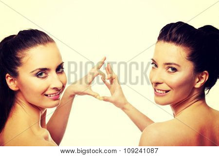 Two beautiful women making heart with fingers.