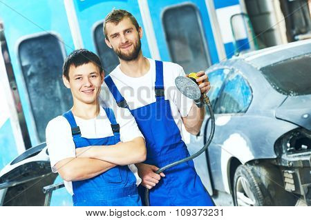 portrait of two smiling auto mechanic workers with power buffer machine  at automobile repair and renew service station