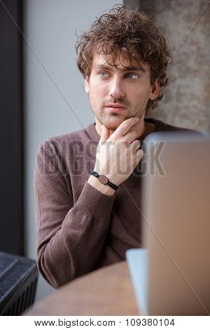 Thoughtful attractive handsome curly pencive distracted guy in brown sweetshirt sitting and dreaming