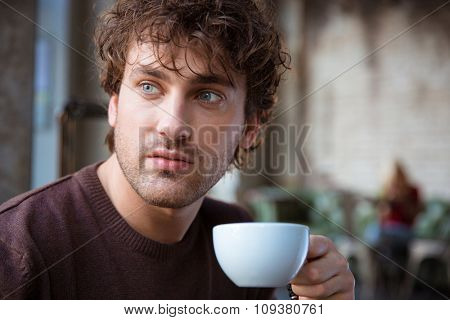 Closeup of handsome attractive thoughtful contemplative curly male drinking coffee
