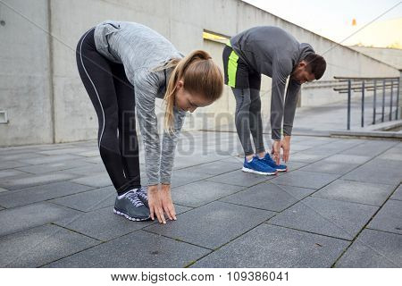 fitness, sport, exercising, people and lifestyle concept - couple stretching and bending forward on street