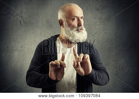 senior bearded man showing refusal sign and looking at camera over dark wall