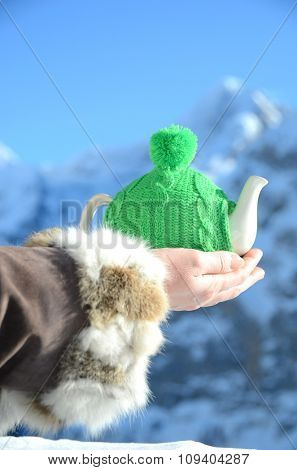 Tea pot in the knotted cap in the hand against alpine scenery