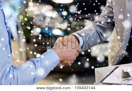 auto business, car sale, deal, gesture and people concept - close up of male handshake in auto show or salon over snow effect